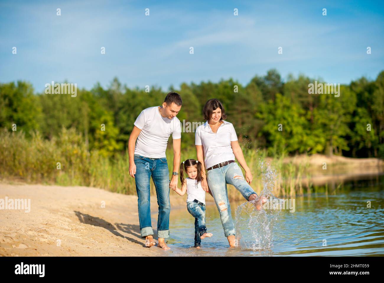 A happy family walks along the riverbank on a sunny day, will barefoot on the water and splash Stock Photo