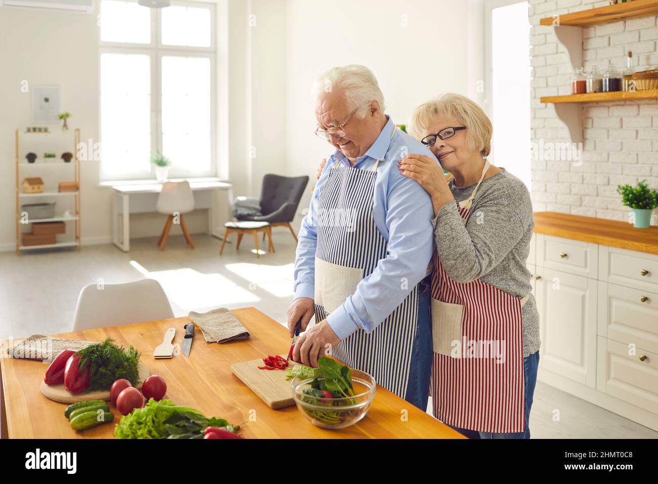 Happy loving elderly couple in aprons cooking healthy vegetarian dinner