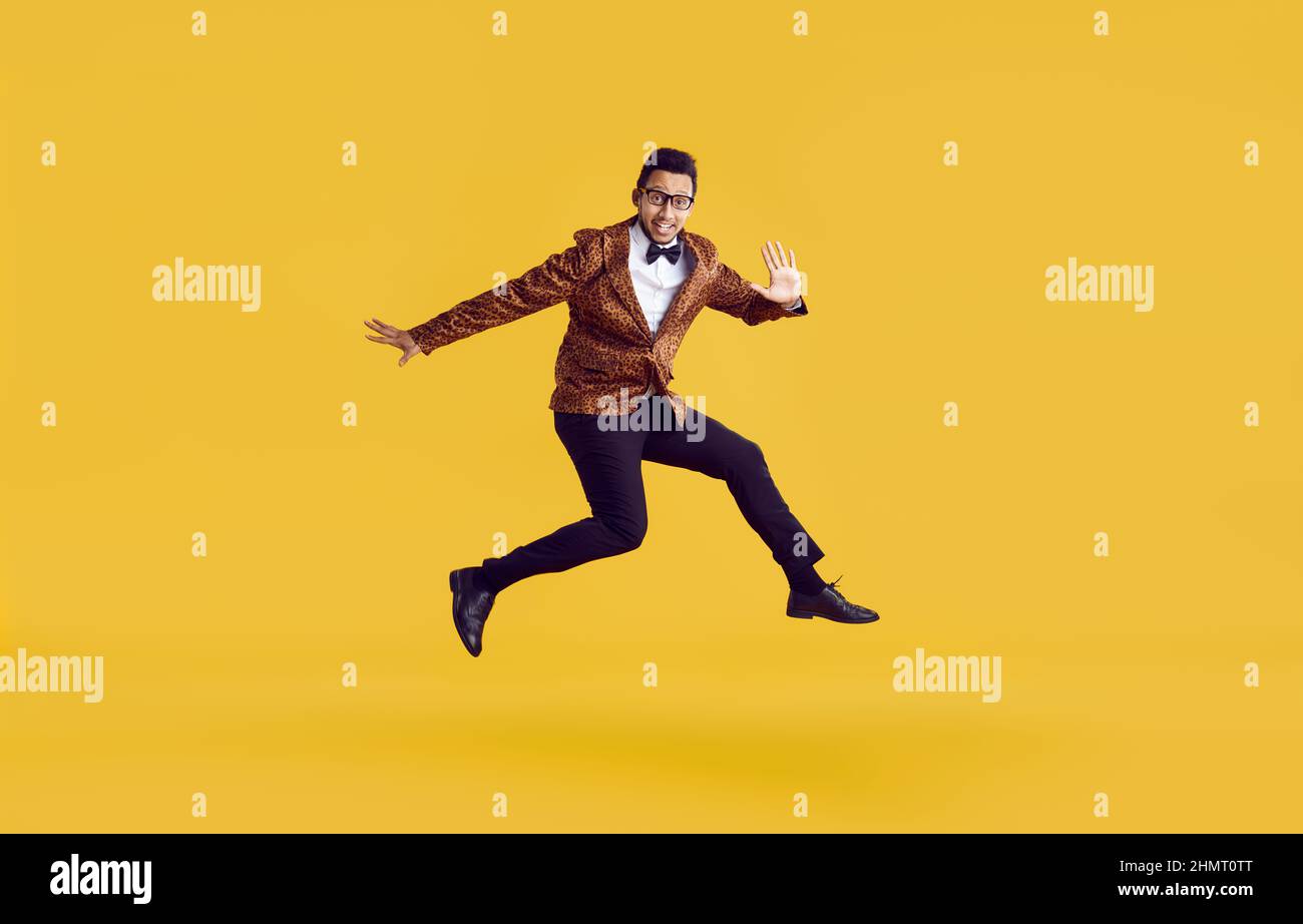 Happy funny young guy in leopard jacket jumping in air isolated on yellow background Stock Photo