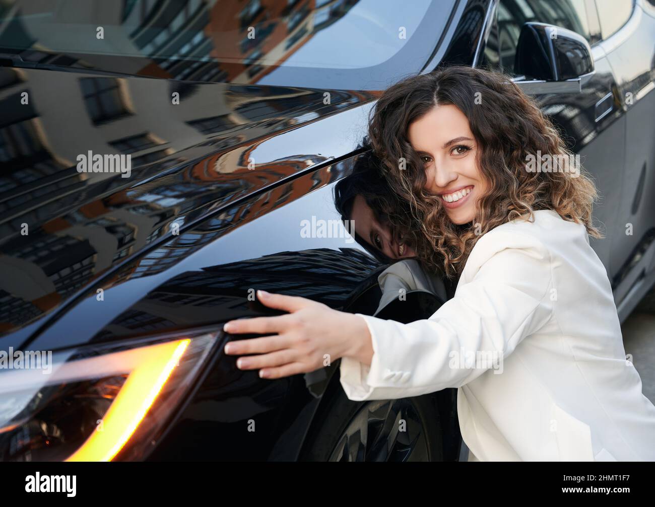 Portrait of happy female proud CEO posing near black car enjoying time for steering and getting to business destination, cheerful Caucasian employer smiling at camera hug company vehicle Stock Photo