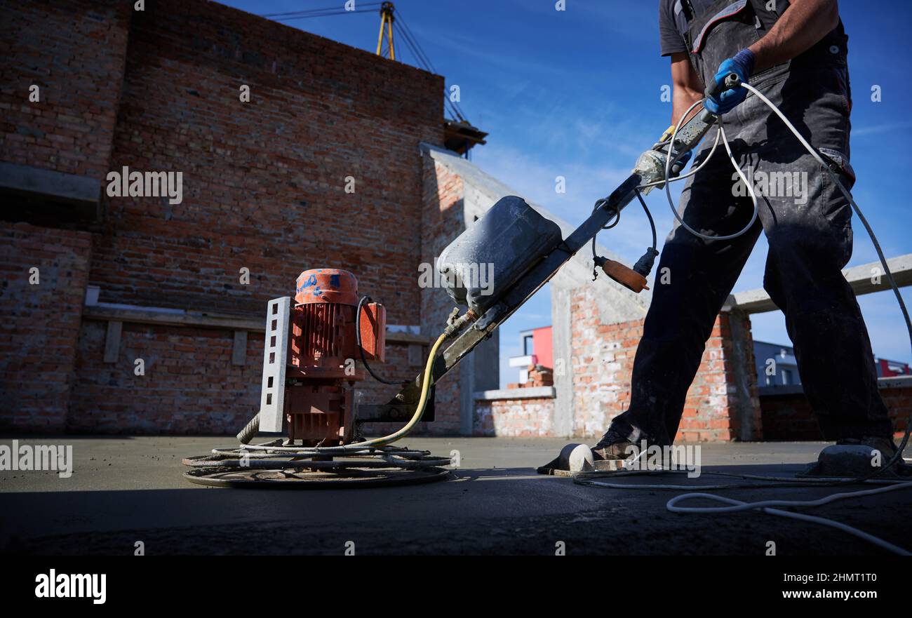 Cropped picture of man laborer in work overalls using power trowel