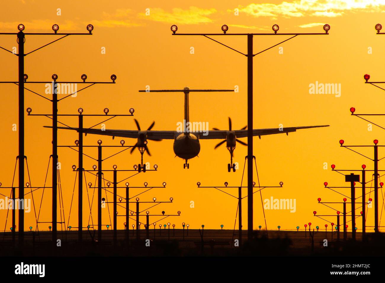 Turboprop aircraft arriving an airport during sunset with the glowing sun and landing lights of the runway Stock Photo