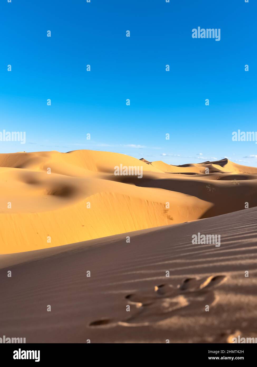 Hand print in the sand on the foreground with yellow golden colored sand dunes and blue cloudy sky in the background. Stock Photo