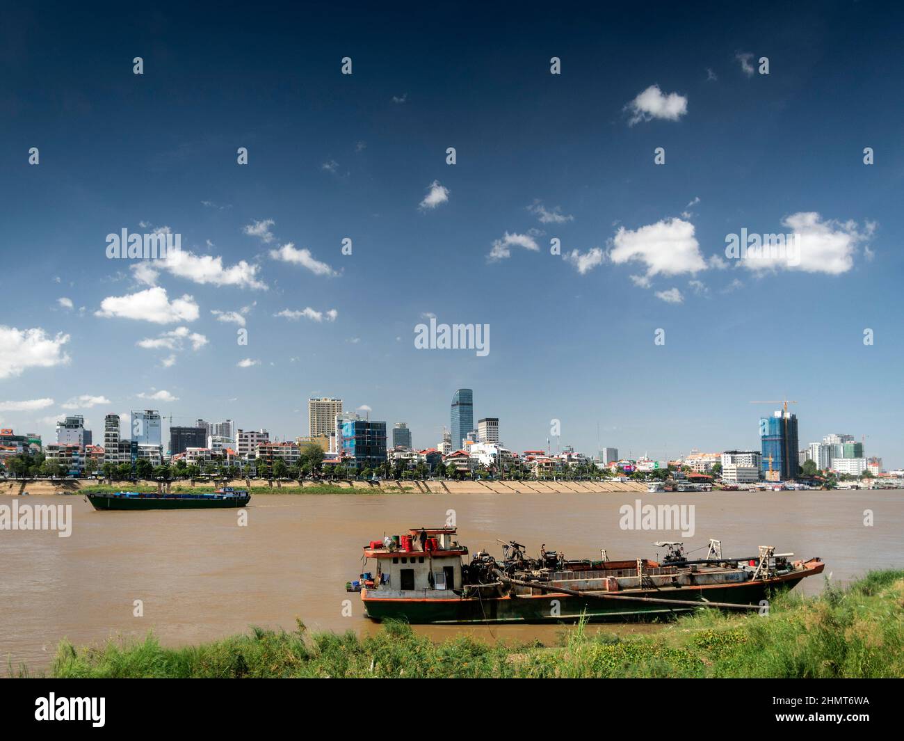 sand dredging boats on the Tonle Sap river with Phnom Penh city skyline in Cambodia Stock Photo