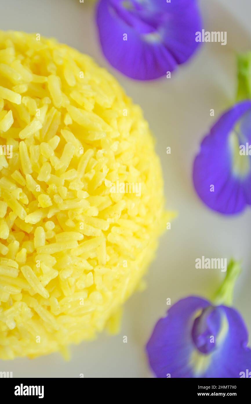 Turmeric Rice and Butterfly pea flowers on white plate. Close-up. Table top view. Stock Photo