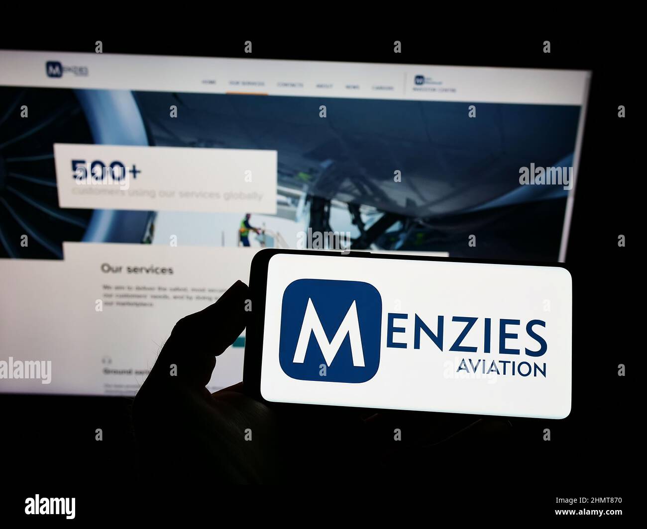 Person holding smartphone with logo of British aviation company John Menzies plc on screen in front of website. Focus on phone display. Stock Photo