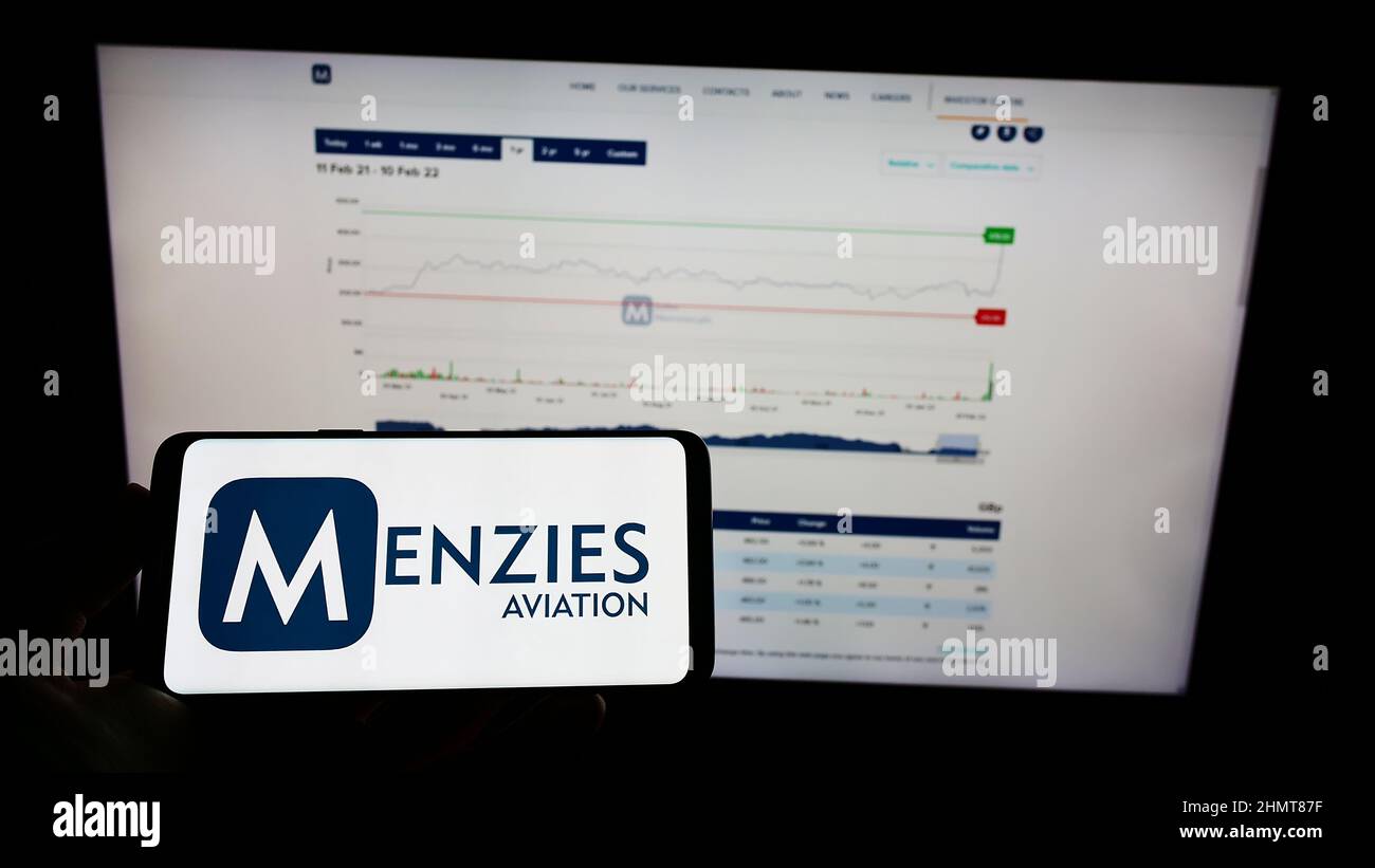 Person holding cellphone with logo of British aviation company John Menzies plc on screen in front of business webpage. Focus on phone display. Stock Photo