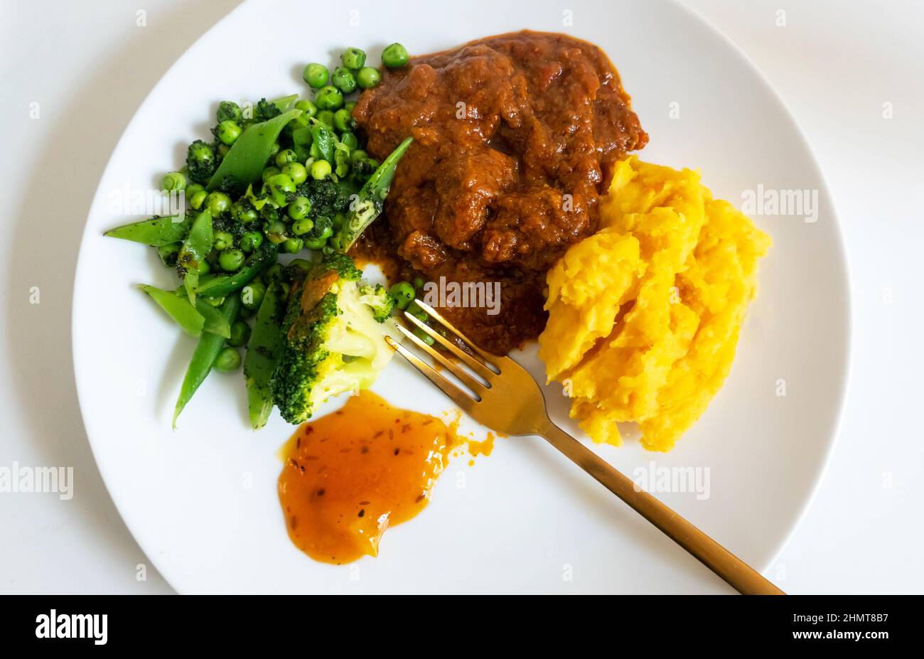Lamb Rogan Josh, a spicy curry with carrot and swede potato and a mix of green vegetables and mango chutney Stock Photo