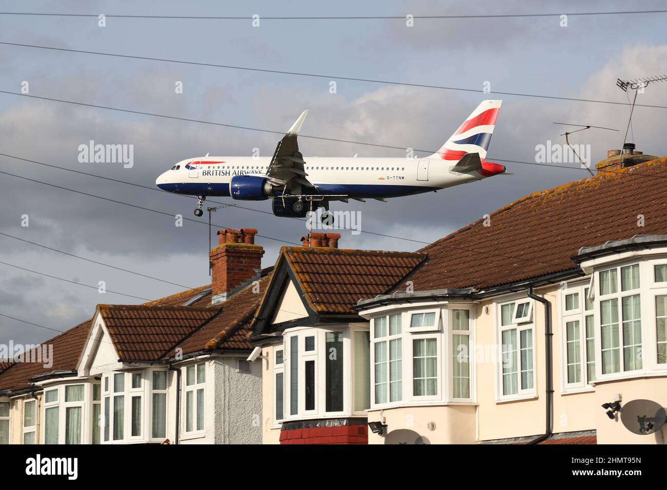 An British Airways Airbus A320neo G-TTNM approaches Heathrow Airport flying low over rooftops of houses in Myrtle Avenue, London, UK Stock Photo