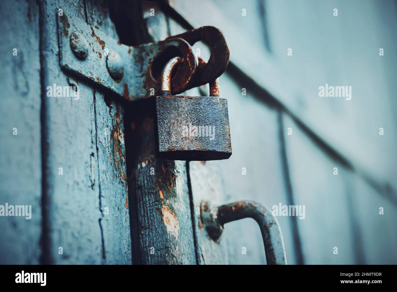 The big blue wooden gate is closed with an old rusty padlock. Tools and household items. The secret is hidden behind the doors. Closed. Stock Photo
