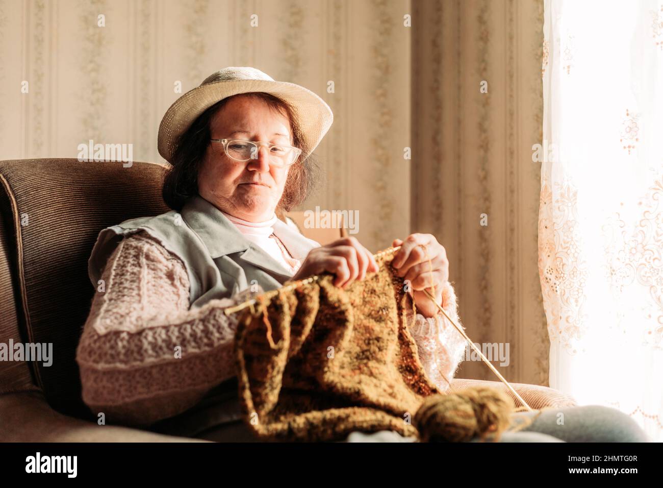 Elderly woman knitting sweater for her grandchildren by the window ...
