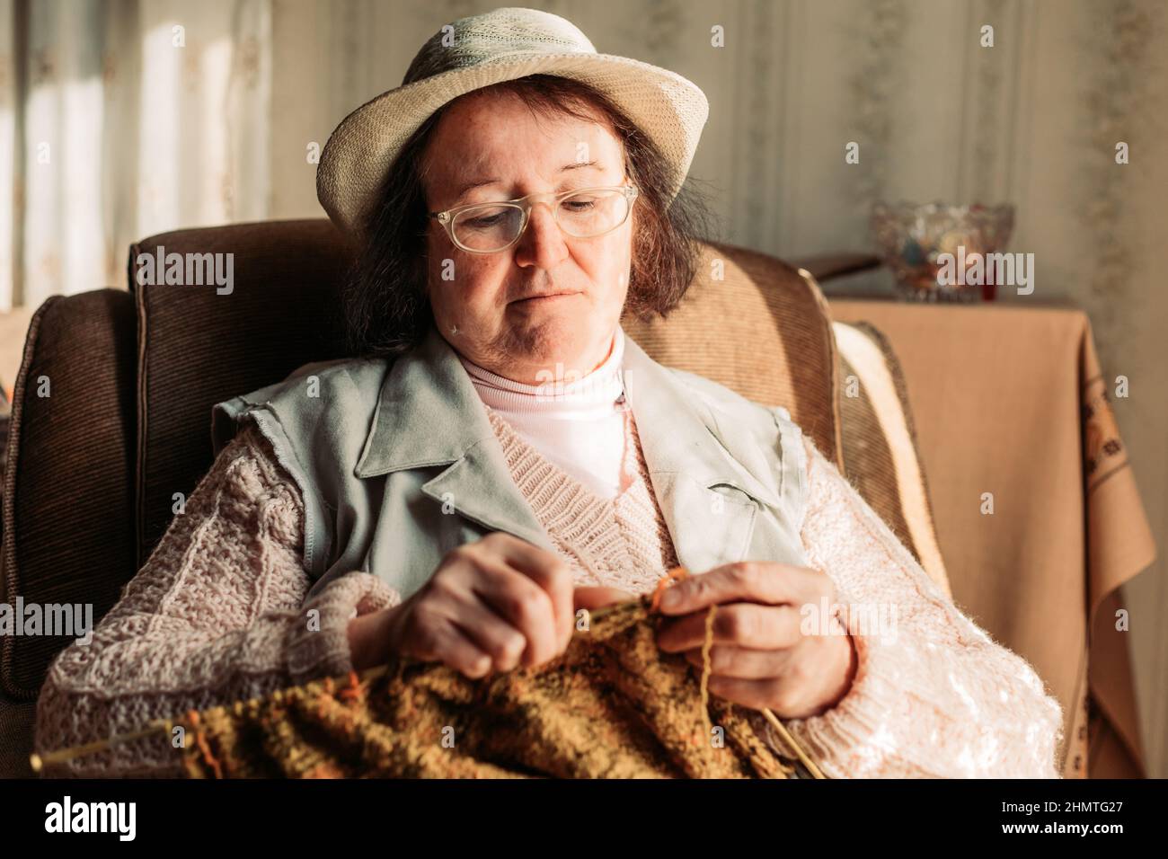 Elderly woman knitting sweater for her grandchildren by the window ...