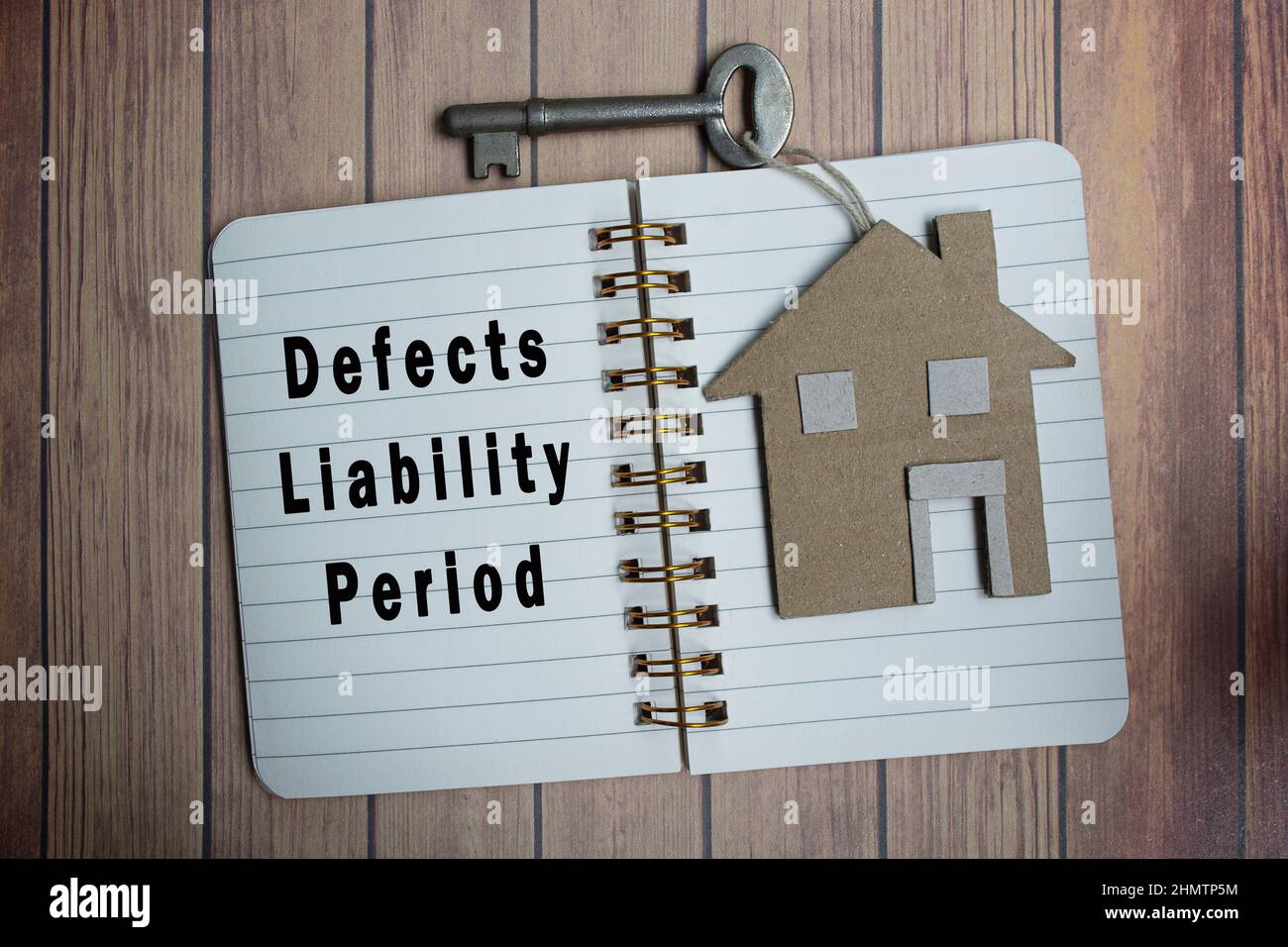 Defects liability period text on notepad with house model and key on wooden desk. Directly above. Flat lay for text. Property management concept. Stock Photo