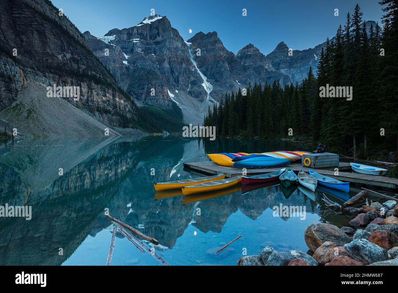 Canoes on a jetty at Moraine lake, Banff national park in the Rocky Mountains at night with moon, Alberta, Canada Stock Photo