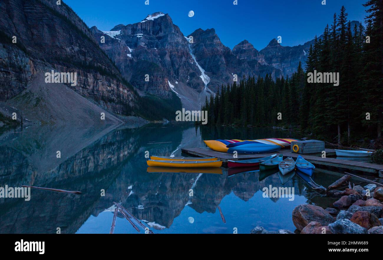 Canoes on a jetty at Moraine lake, Banff national park in the Rocky Mountains at night with moon, Alberta, Canada Stock Photo