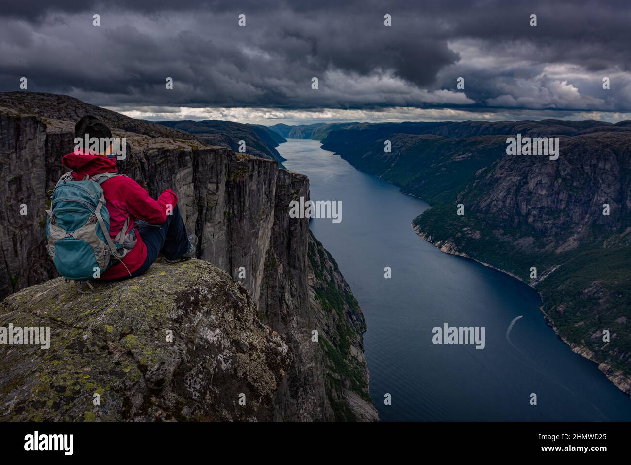 Backpacker sits on top of the Eagle Head Viewpoint near Kjeragbolten Stock Photo