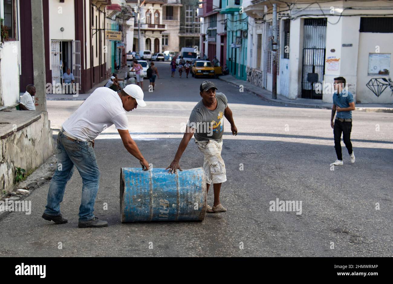 Two men working, one wearing a Simpsons cartoon t'shirt, push a heavy can through the streets of Havana, Cuba. Stock Photo