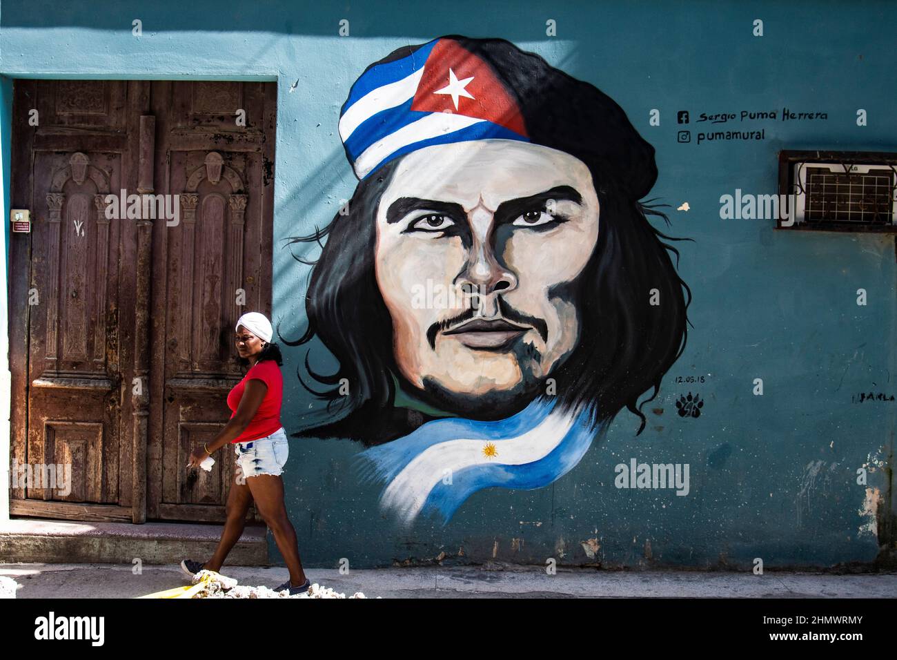 Woman walking the street in Havana, Cuba in front of a graffiti artistic image by artist Pumamural of legendary revolutionary hero Che Guevara. Stock Photo