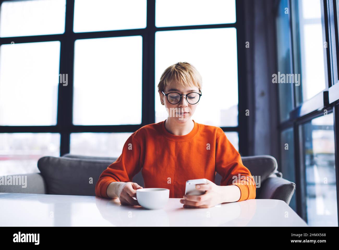 Thoughtful woman with cup of coffee using smartphone Stock Photo