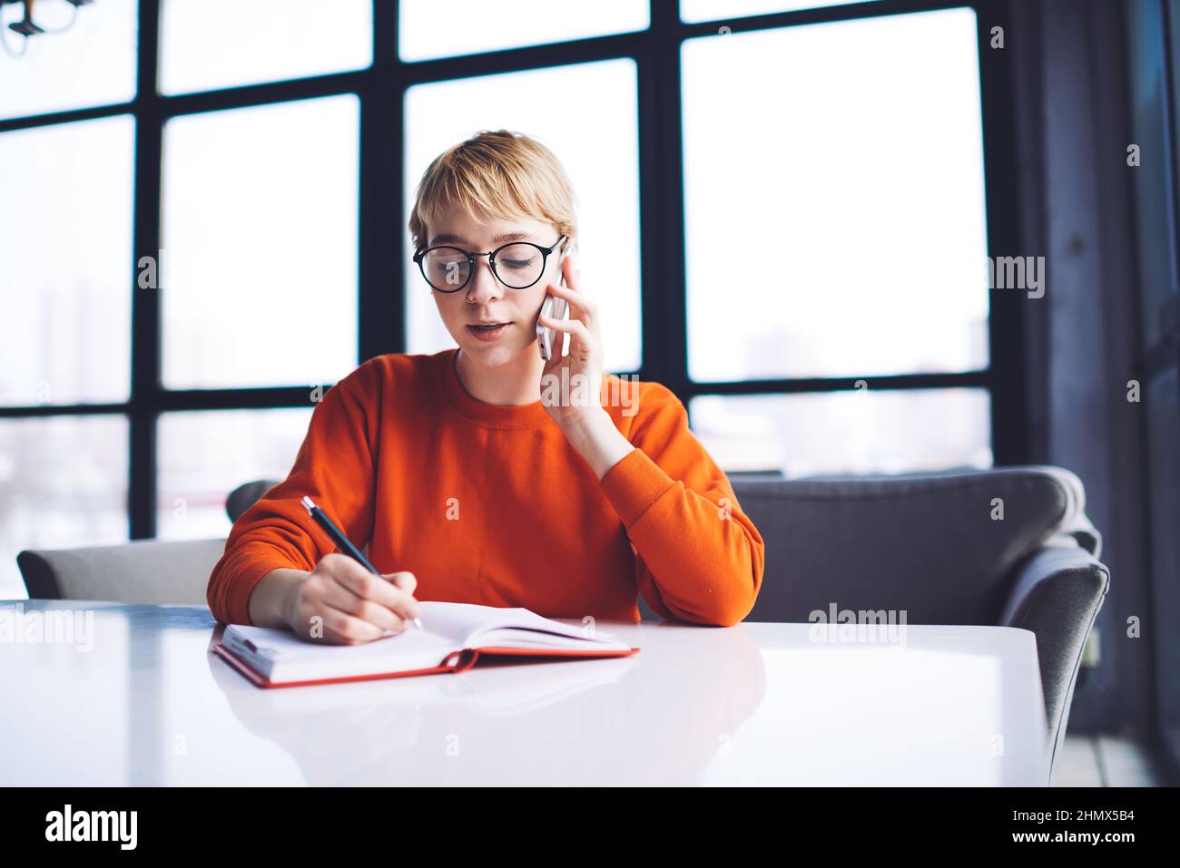 Thoughtful woman writing notes while making phone call Stock Photo