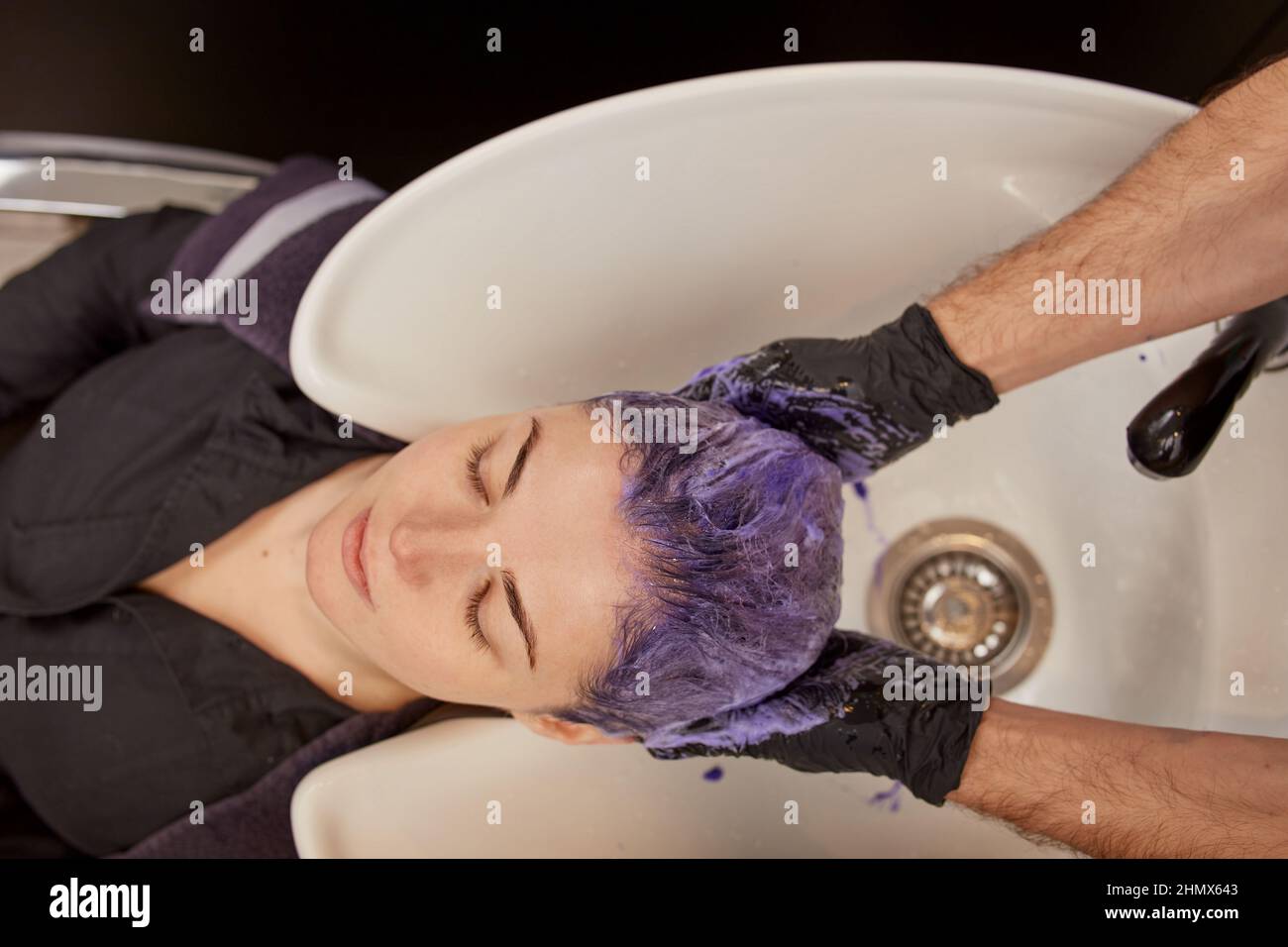 Hairdresser applying purple toning shampoo on woman hair Stock Photo