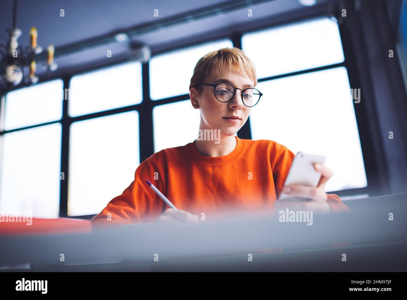 Student reading message on smartphone doing homework sitting at table Stock Photo