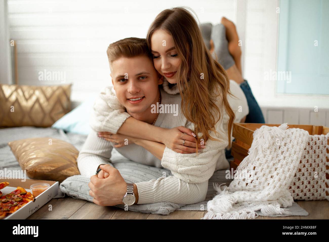 Portrait of young beautiful couple who arranged home date . Young woman hugs her lover, they are lying on floor on blanket in room. Creative date Stock Photo