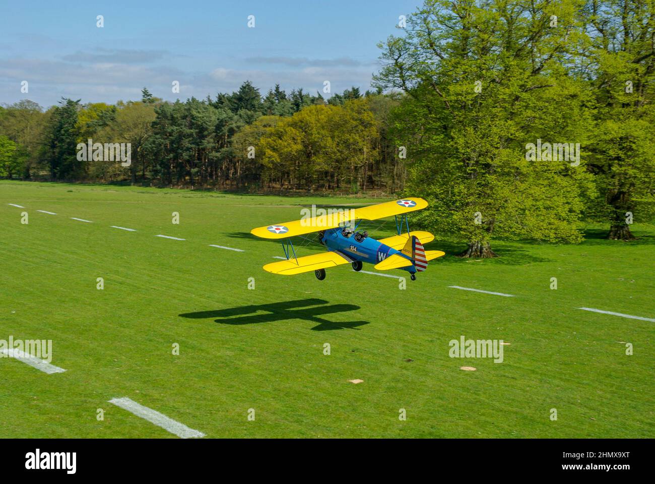 Boeing Stearman biplane N4712V, trainer plane taking off from Henham Park countryside grass strip. Tree lined Suffolk grass runway on sunny summer day Stock Photo