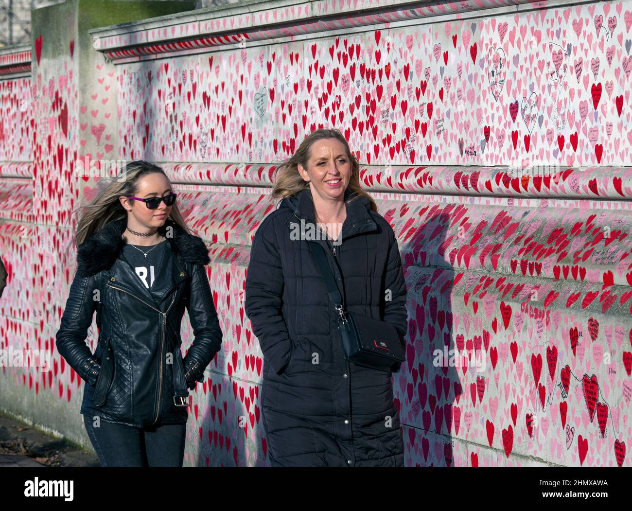 To woman passing the National COVID Memorial Wall painted with red hearts on beautiful sunny day . Westminster, London , UK . Stock Photo