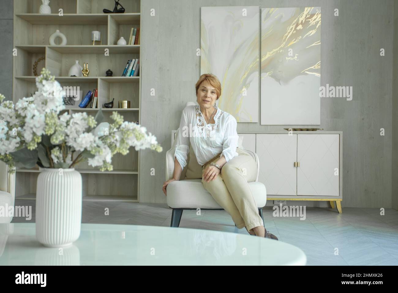 Smiling mature woman sitting on armchair in living room at home Stock ...