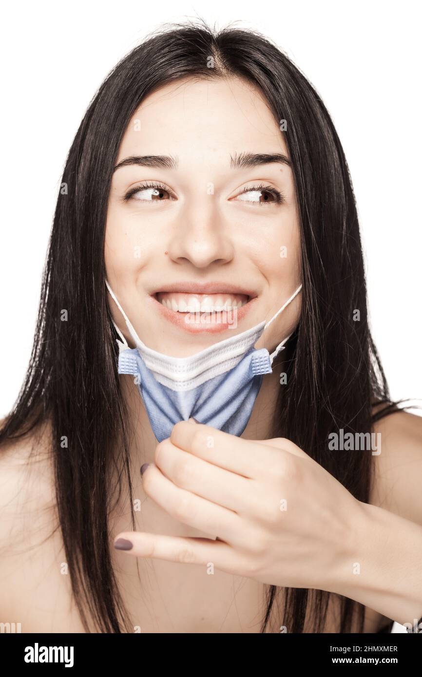 Happy girl pulling away medical face mask. Portrait against white background. Stock Photo