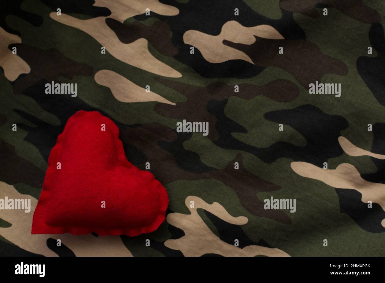 Red heart on military camouflage uniform with copy space. Love and war concept Stock Photo