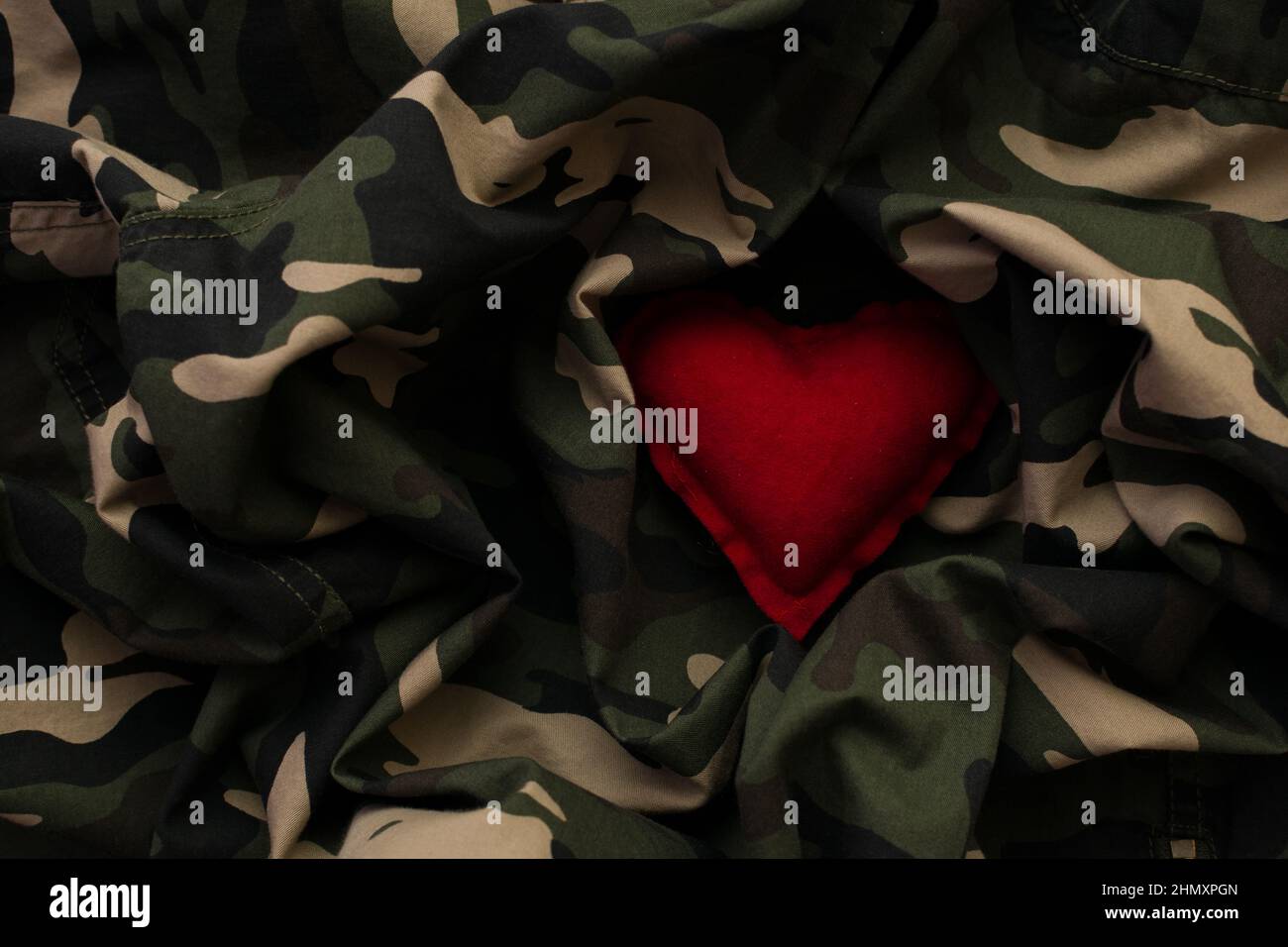Red heart on military camouflage uniform. Love and war concept Stock Photo