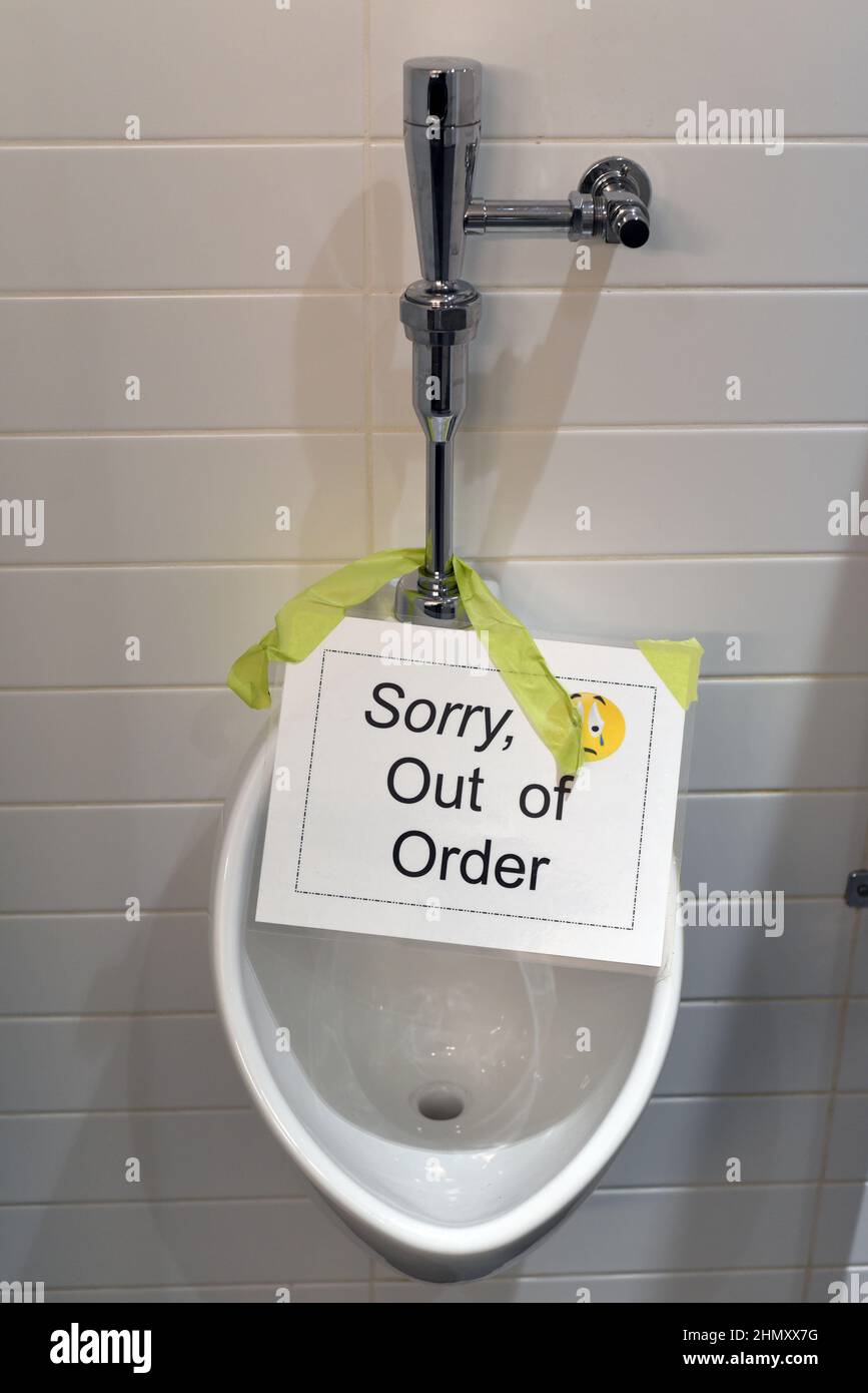 A broken urinal with a sign saying “Sorry, out of order” in a men’s