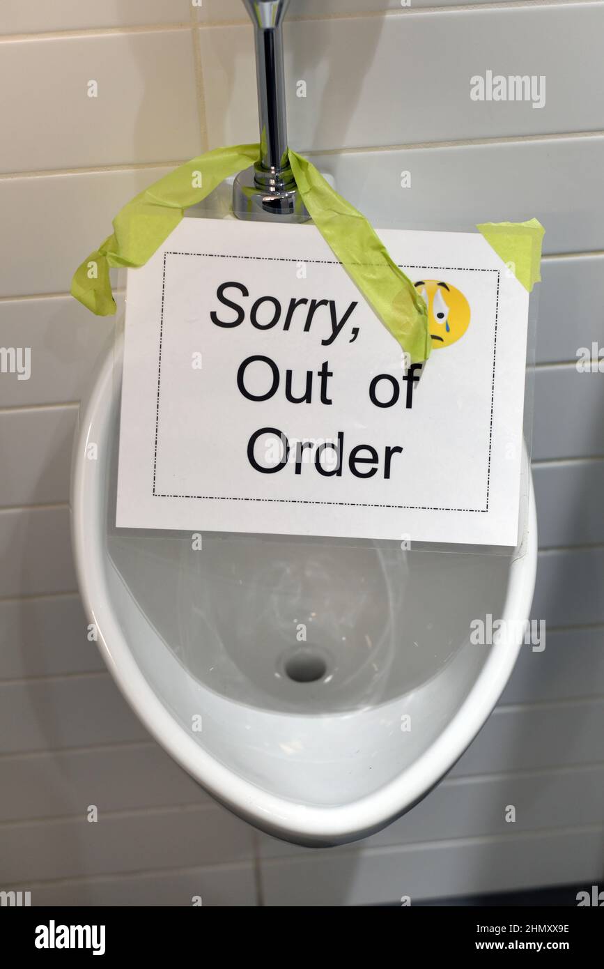 A broken urinal with a sign saying “Sorry, out of order” in a men’s