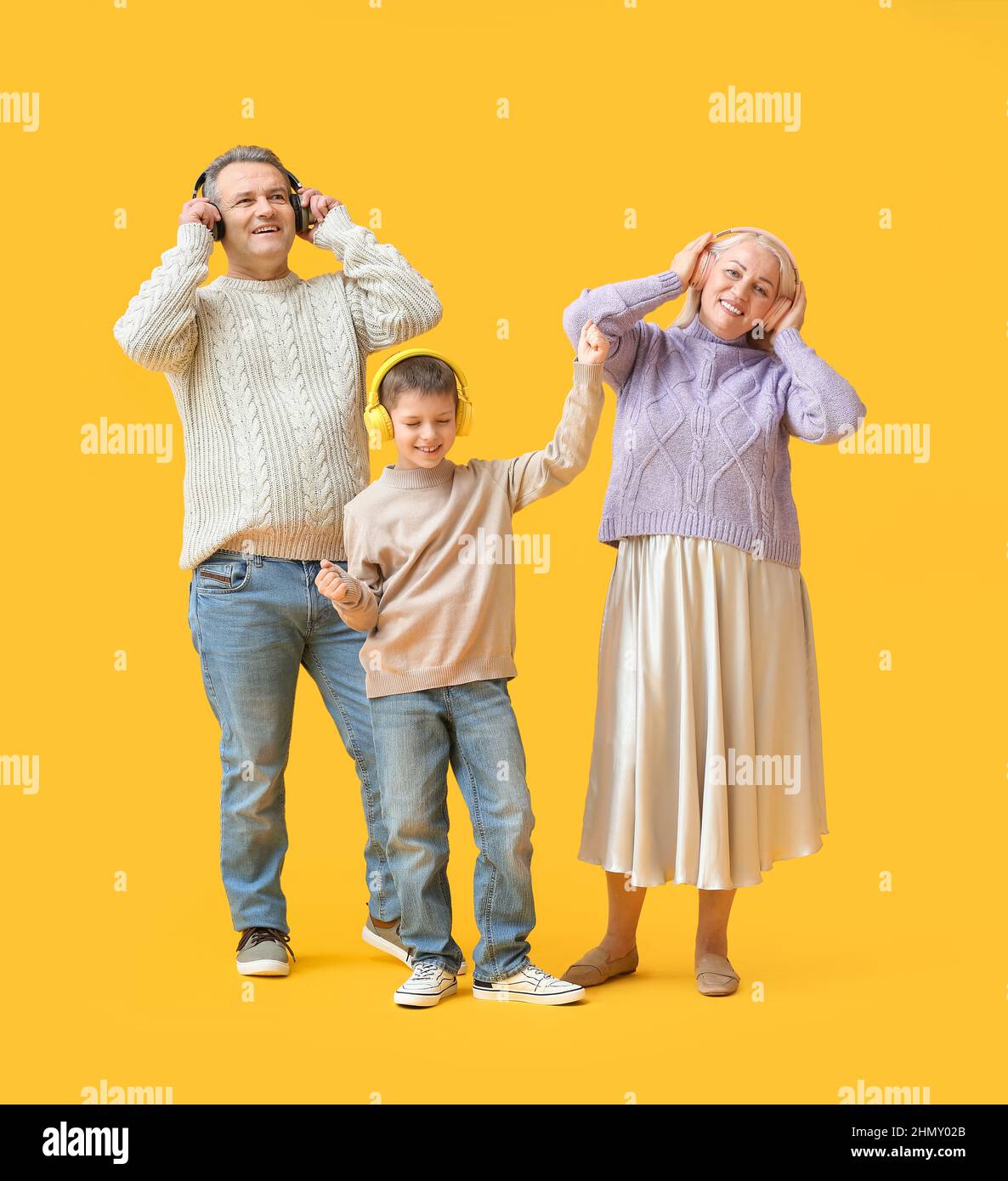 Little boy with his grandparents in warm sweaters and headphones on yellow background Stock Photo