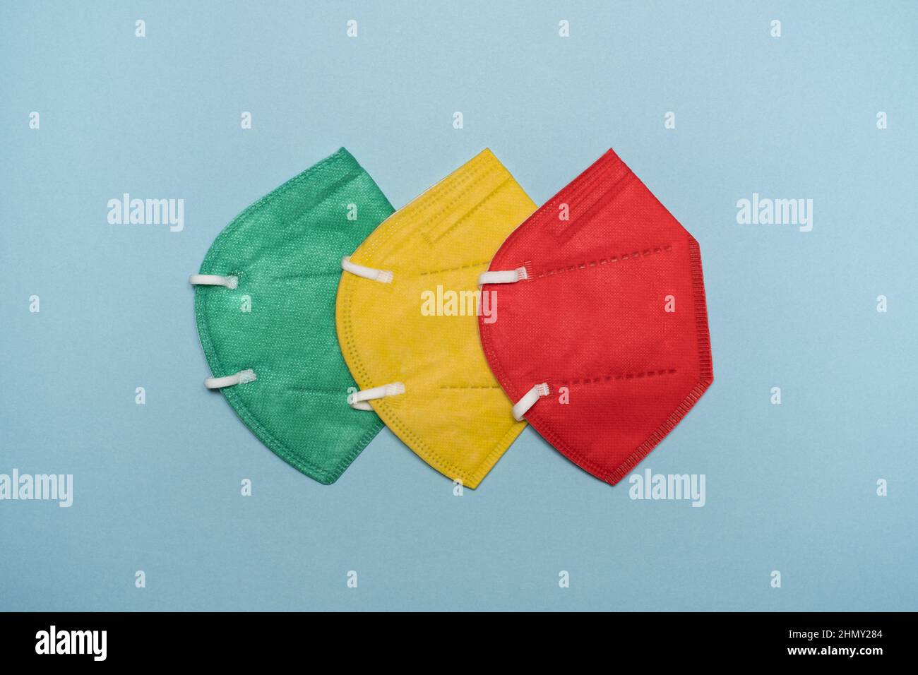 The Concept of Traffic Light System shows the phase of the pandemic Covid lockdown. Red, yellow and green respirator protective masks on blue bg. Stock Photo