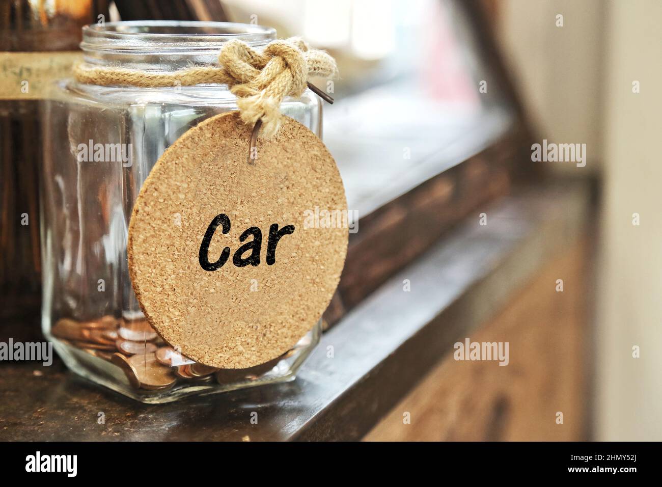 Saving money for buy car. Vintage retro glass jar with hemp rope tie Car tag and few coins inside on wood counter. spending on down payment interest. Stock Photo