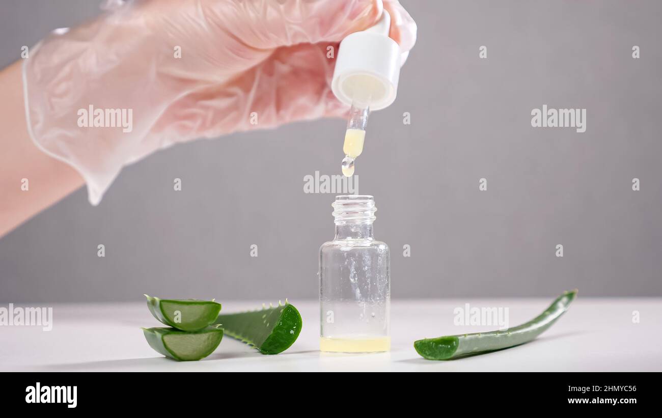 Specialist drops aloe juice into glass bottle on white table Stock Photo