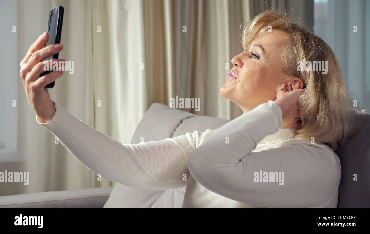 Elderly blonde woman takes selfies using cellphone Stock Photo