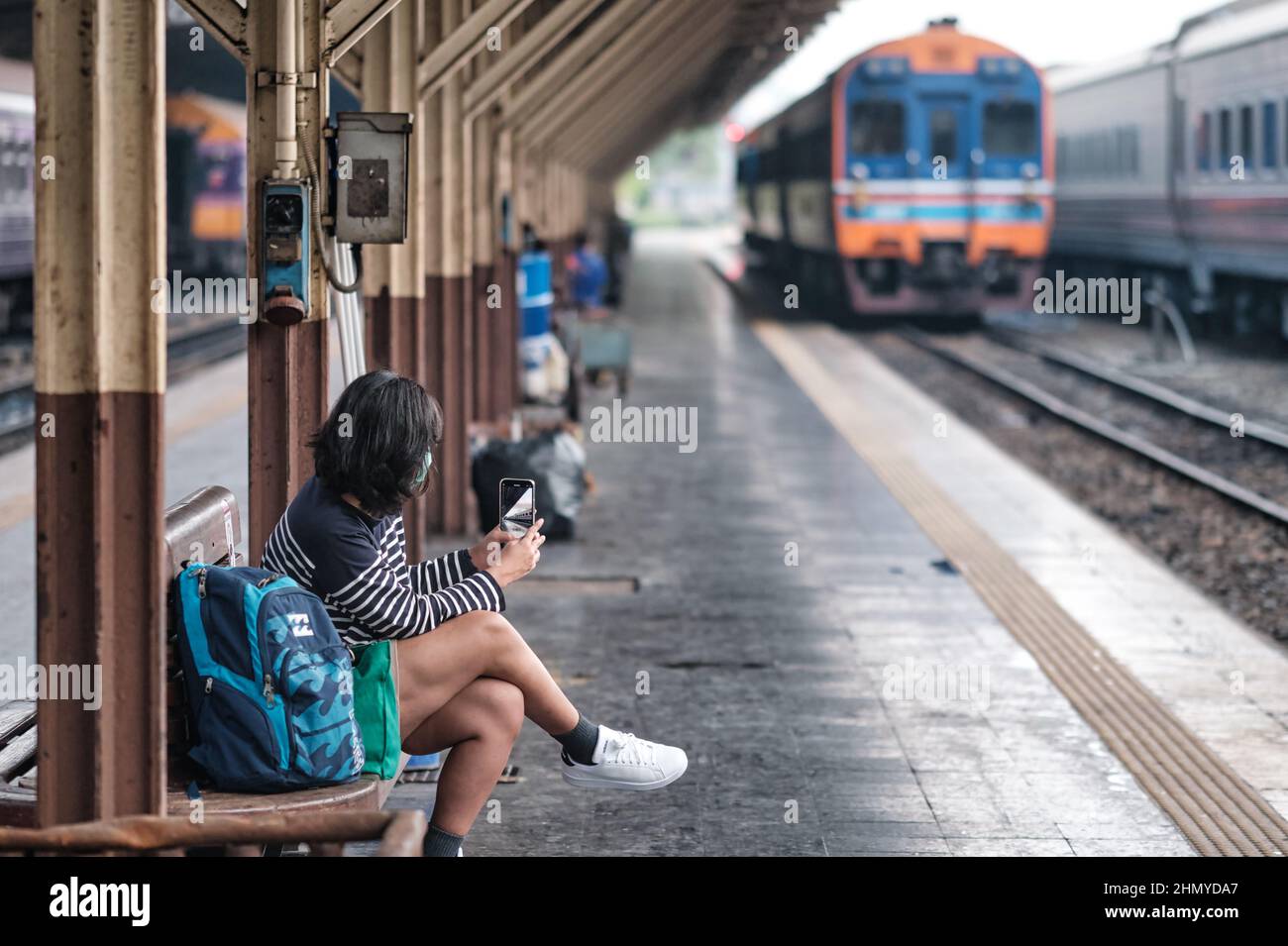 A young female passenger on a platform at Hualamphong (Hua Lamphong) Station in Bangkok, Thailand, taking photos on her mobile of her incoming train Stock Photo