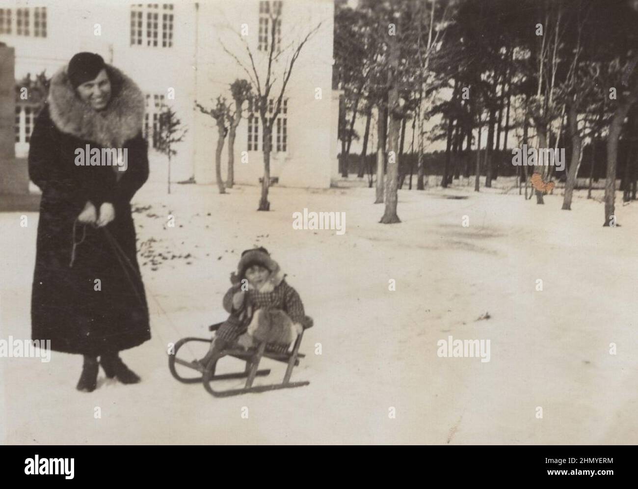 vintage family photo from the 1930s. Middle class mother standing with her son at winter time. The mother is wearing a big coat with massive red fox fur  scarf and the little boy is sitting on his sledge. source: original photographs ADDITIONAL-RIGHTS-CLEARANCE-INFO-NOT-AVAILABLE Stock Photo