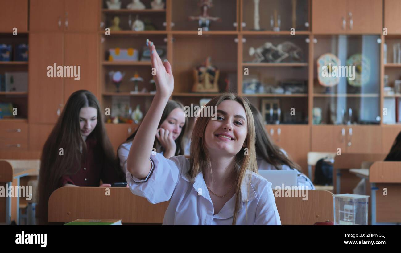 A girl student sitting at a desk raises her hand in the class Stock ...