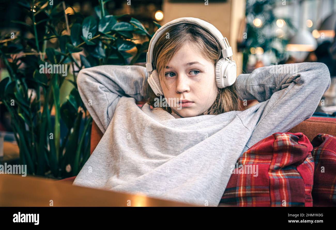 A cute little girl is sitting on the couch wearing headphones Stock ...