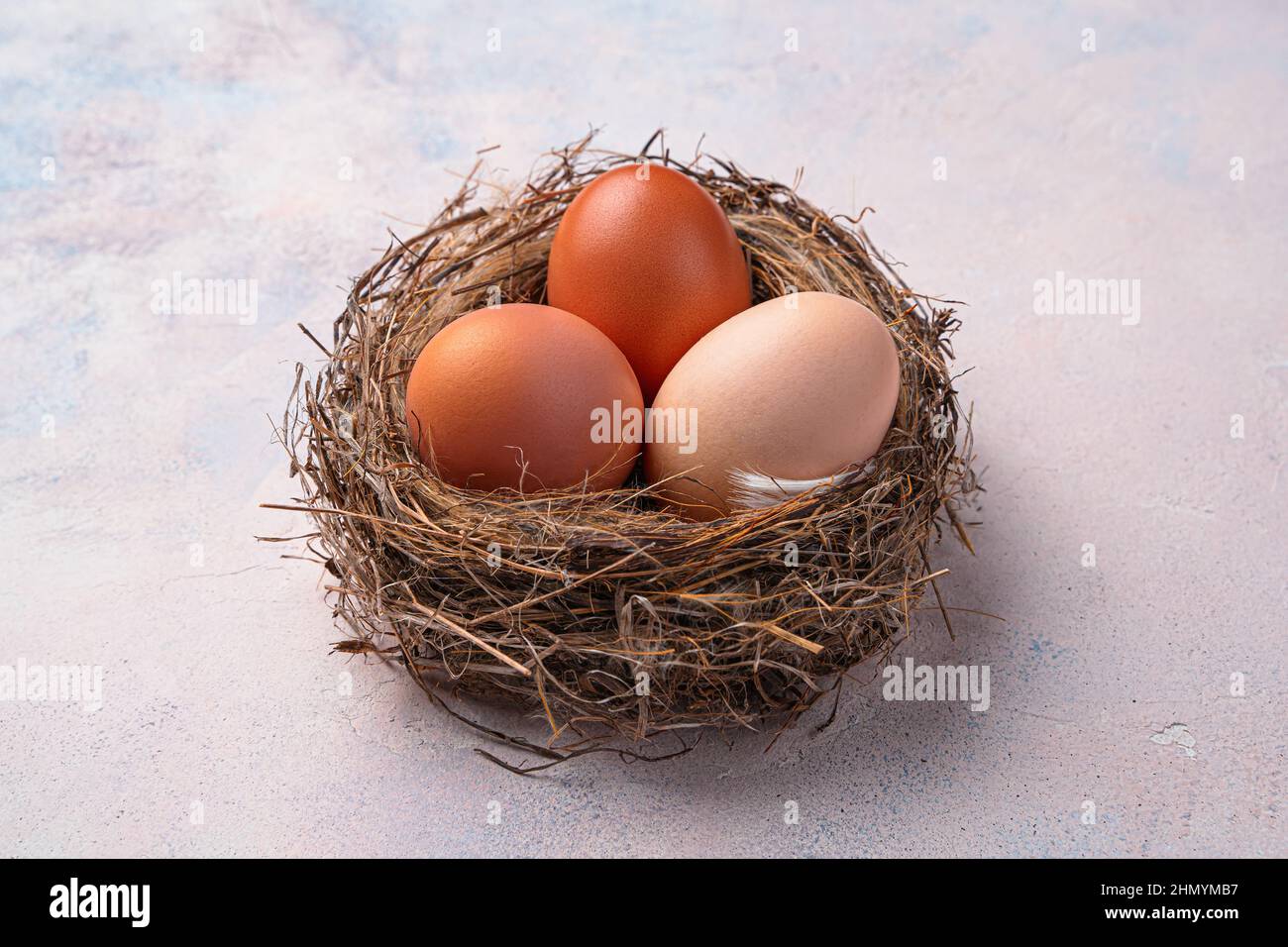 Three chicken eggs in a nest on a light background. Top view, close-up. Stock Photo