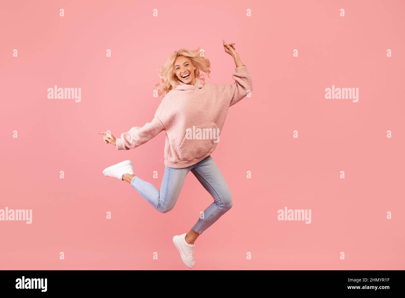 Having fun. Full body length portrait of playful lady jumping, dancing and smiling at camera, being in a good mood Stock Photo