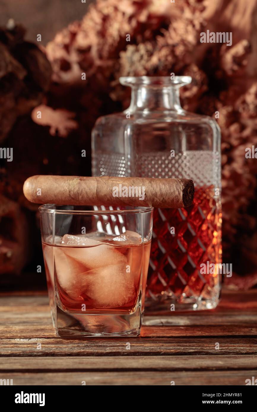 Whiskey with ice and cigar on an old wooden table. In the background are old snags. Copy space. Stock Photo