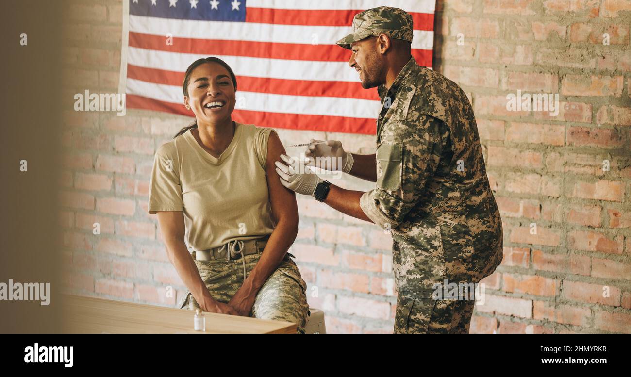 Happy servicewoman receiving a dose of the covid-19 vaccine in the military hospital. American female soldier laughing happily while getting injected Stock Photo