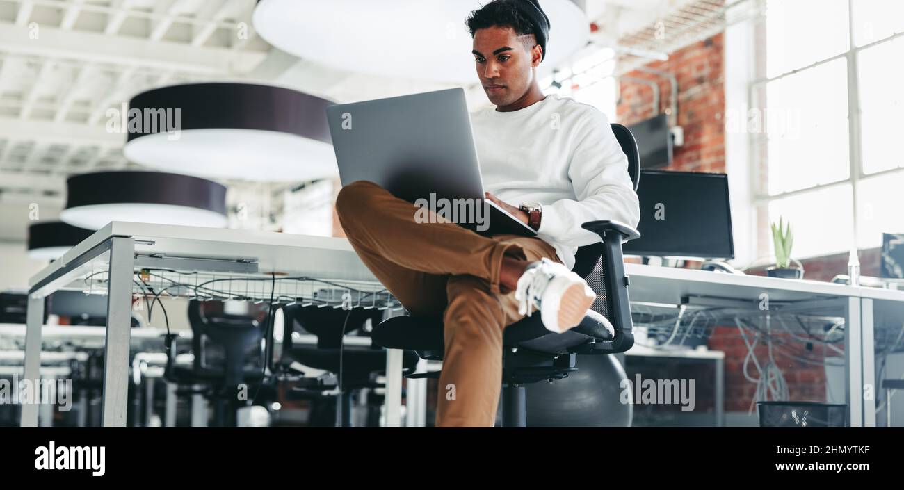 Programmer working on a new project in an office. Focused young businessman using a laptop while sitting in a modern workplace. Creative businessman w Stock Photo