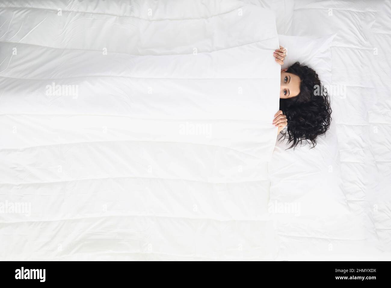 Woman laying on white bedding covering with blanket, wake up well rested in morning Stock Photo